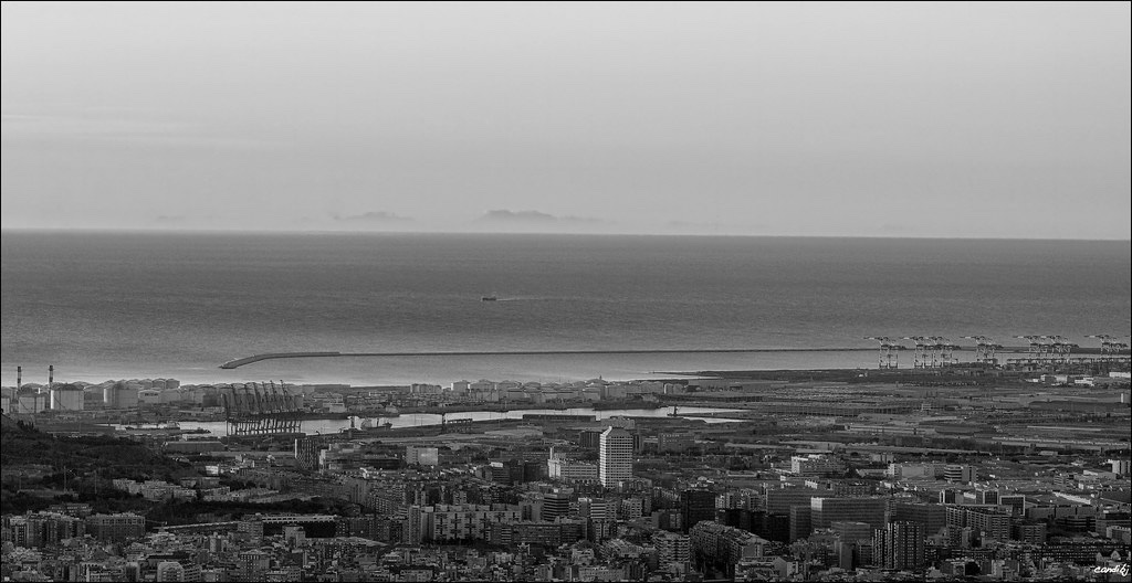 La silueta serrada de la Serra de Tramuntana surant sobre l'horitzó marí més enllà del port de Barcelona, fotografiada a l'alba