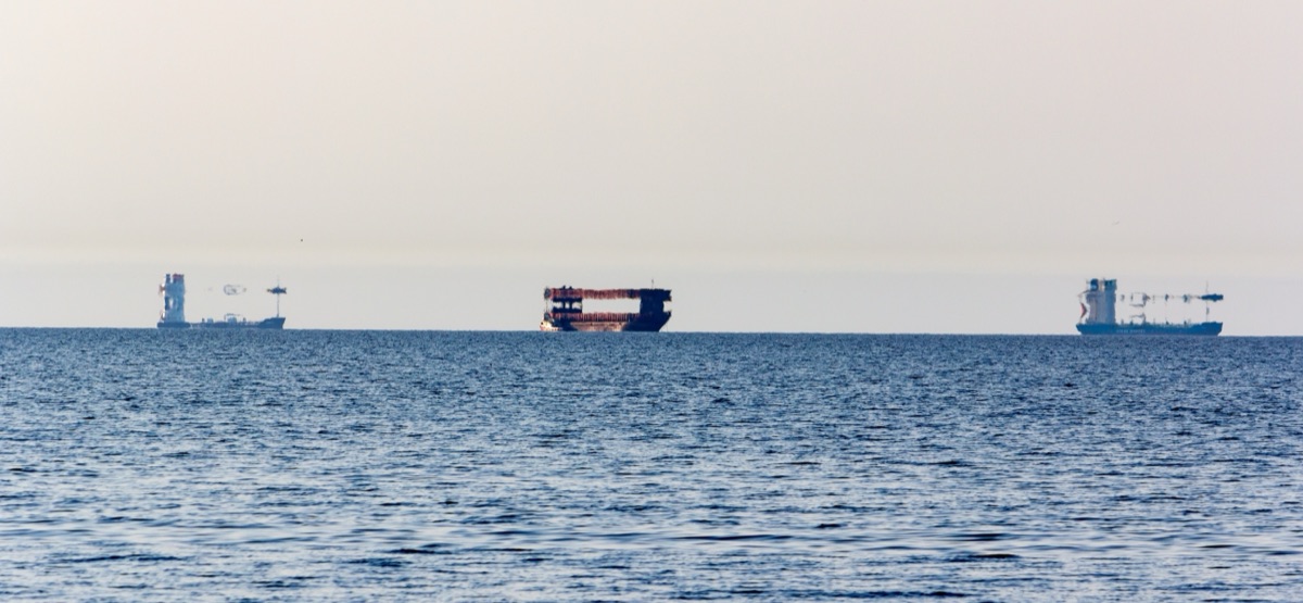 Three cargo ships on the Gulf of Riga distorted by a superior mirage, their hulls stretched vertically and apparently floating above the horizon