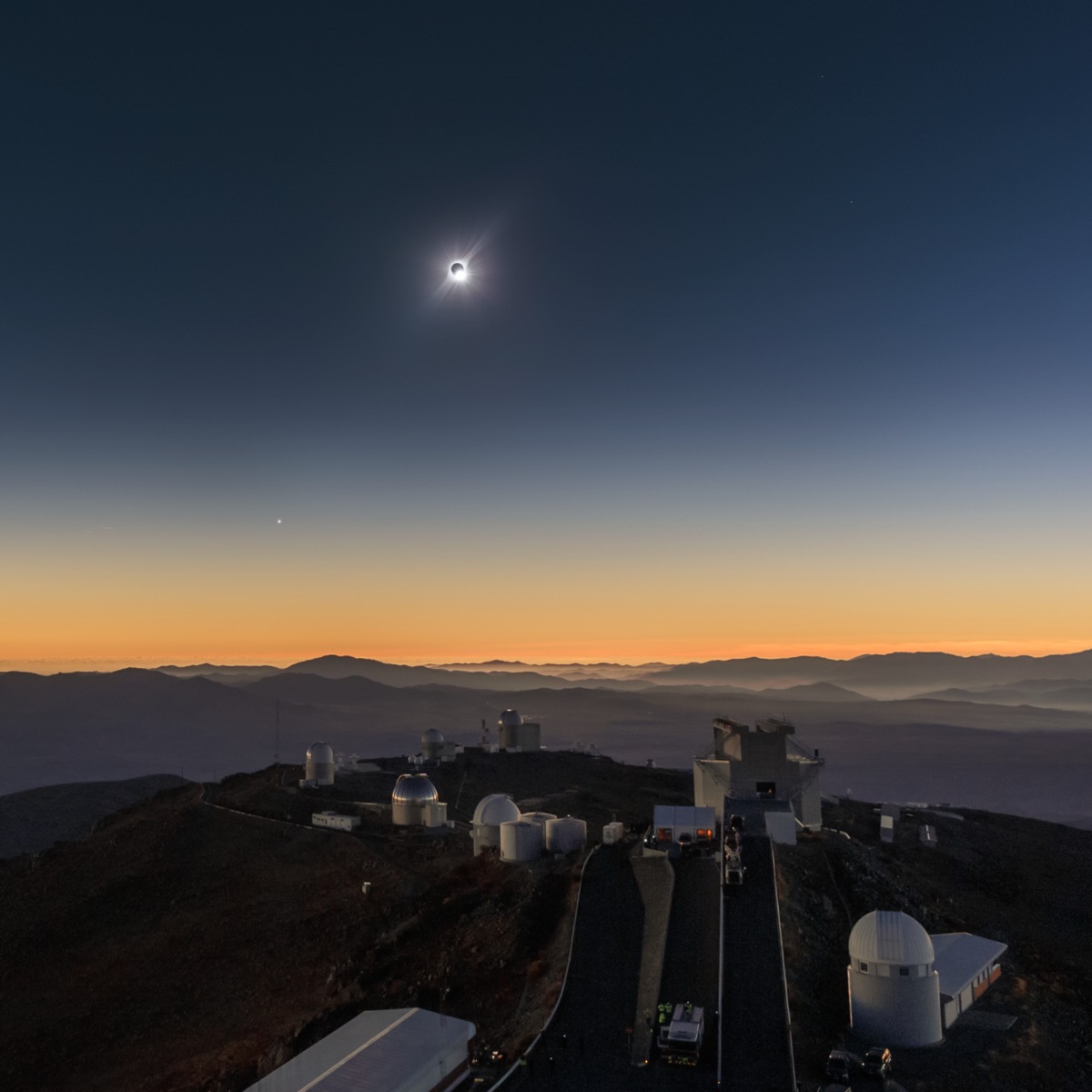 El eclipse total de 2019 visto desde el observatorio de montaña de La Silla: la corona en un cielo oscurecido sobre las cúpulas de los telescopios, con colores crepusculares en todos los horizontes