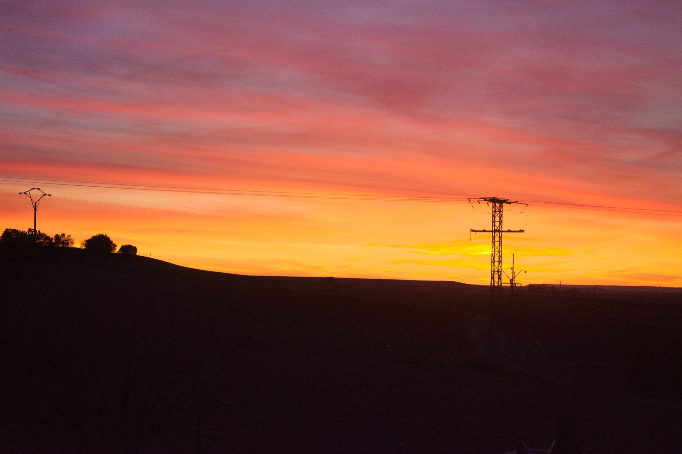 Una plana castellana totalment plana retallada contra un enorme cel de posta de Sol vermell i taronja, un sol pal d'alta tensió i un turonet baix com a únics trets