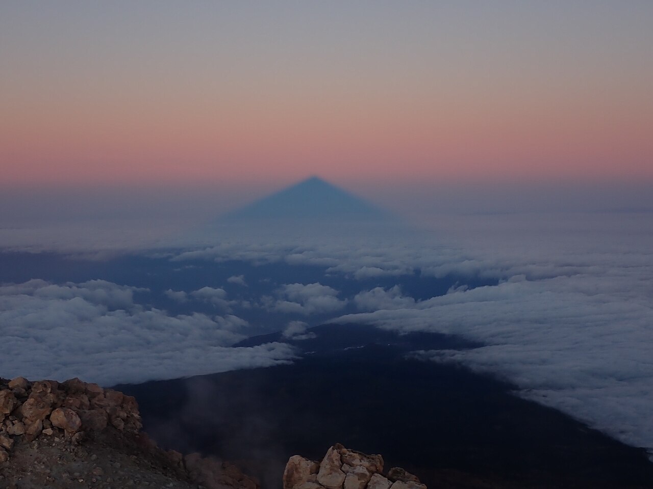 Teide's blue triangular shadow floating in the pink Belt of Venus above a sea of clouds at sunrise